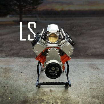 A clean LS engine on a stand in a garage with a sunset background.