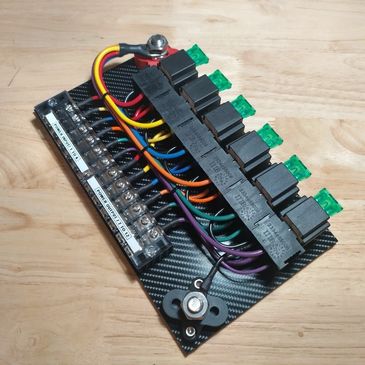 A fuse box with multiple colored wires and green fuses on a carbon fiber plate.