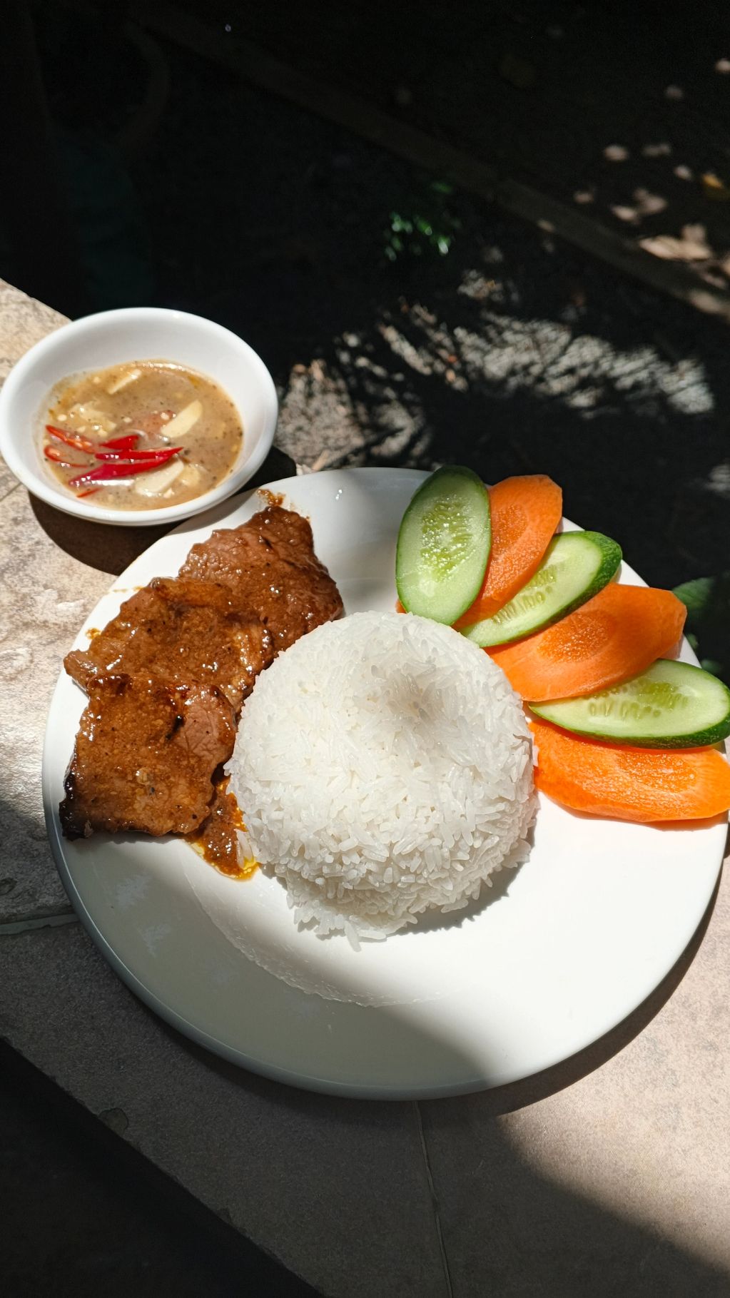 Plate with rice, meat, cucumber, carrots, and a bowl of sauce.