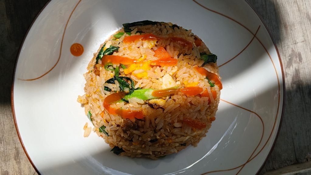 A plate of fried rice with vegetables and sauce.