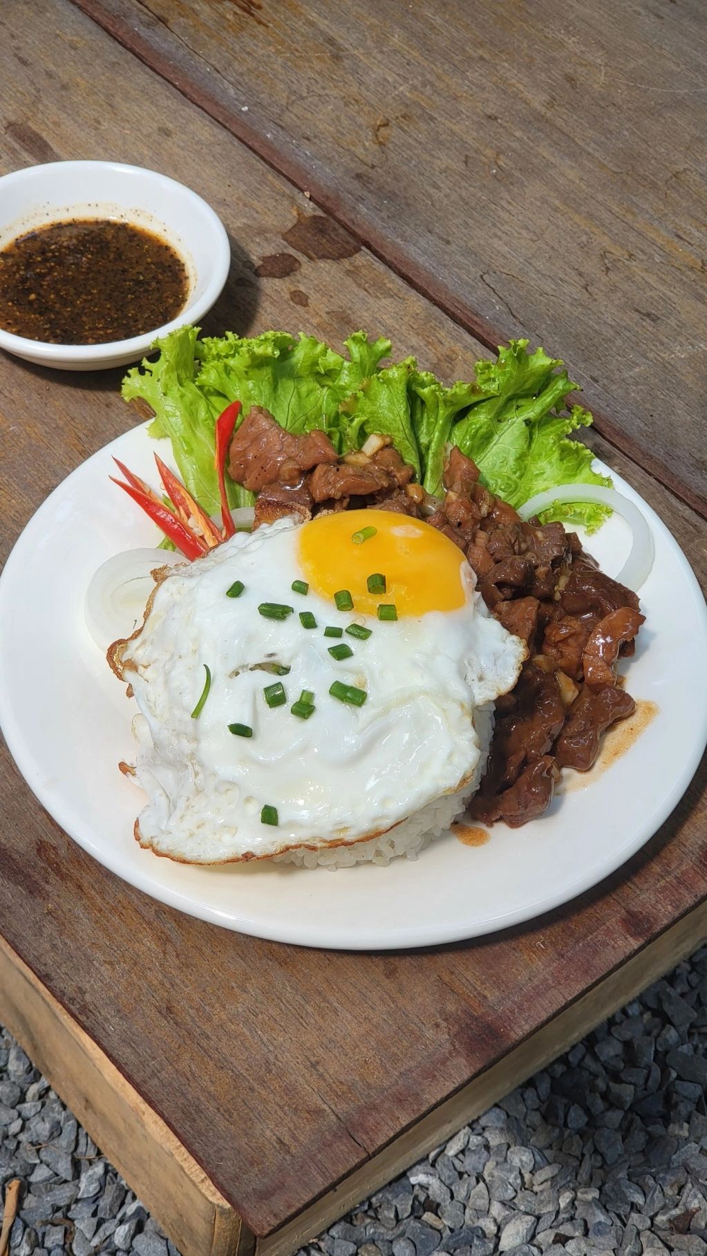 Plate of rice topped with fried egg, beef, lettuce, and chili with dipping sauce.