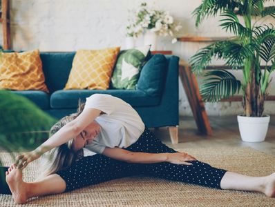 Woman stretching on floor in cozy living room with plants and sofa.