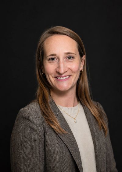 Professional woman smiling against a black background in business attire.