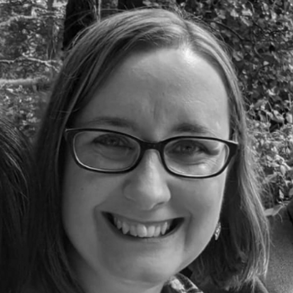 Black and White image of Roxy. Smiling with glasses and shoulder length hair. 