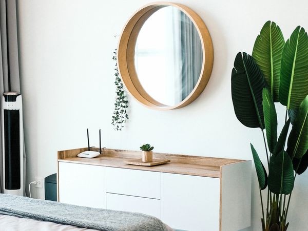 End of bed with round mirron on wall and plant