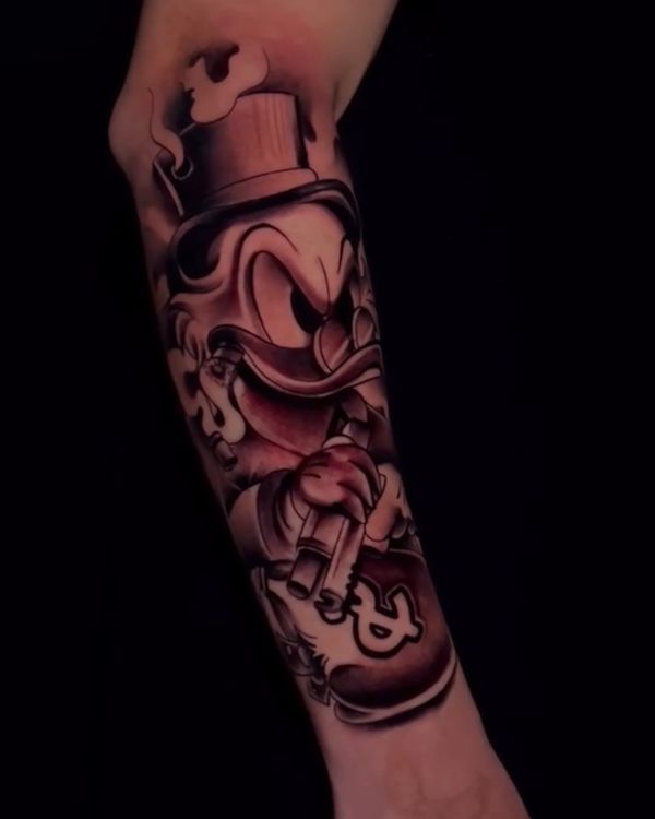Tattoo of a cartoon duck with a top hat, cigar, and money bag on forearm.