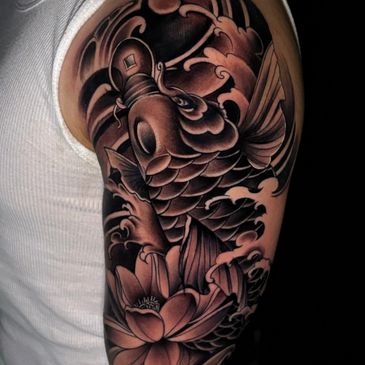 Black and gray koi fish tattoo with water and lotus flower on upper arm.