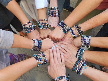 Group hands together wearing colorful beaded bracelets, symbolizing unity and friendship.