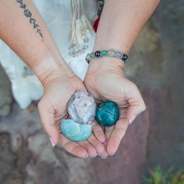 Hands holding polished stones and crystals outdoors.