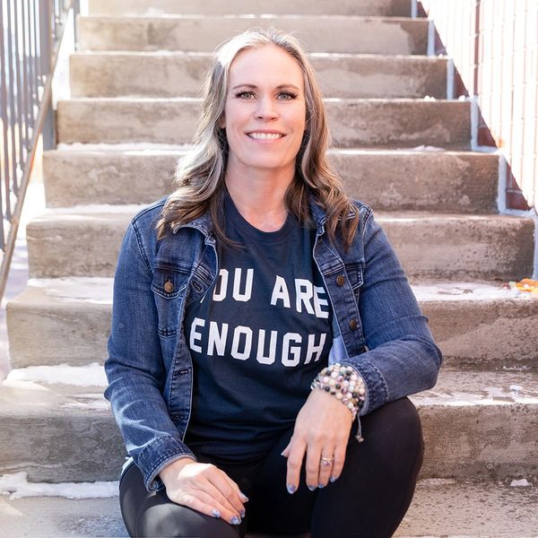 Woman sitting on stairs wearing a shirt that says 'You Are Enough'.