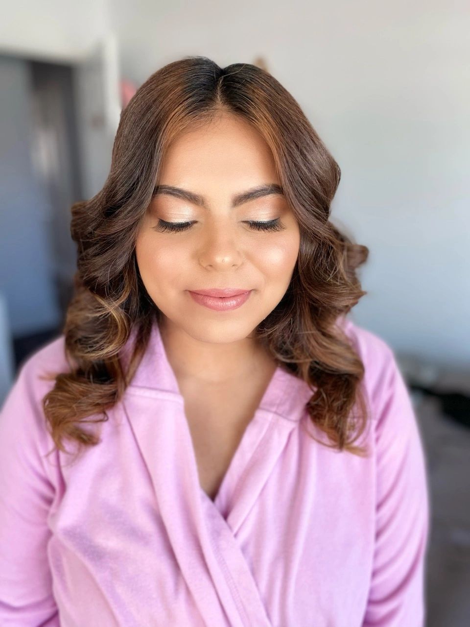 Woman with curled hair and soft makeup wearing a pink robe.