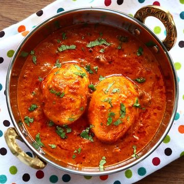 Egg curry garnished with fresh herbs in a brass-handled bowl.