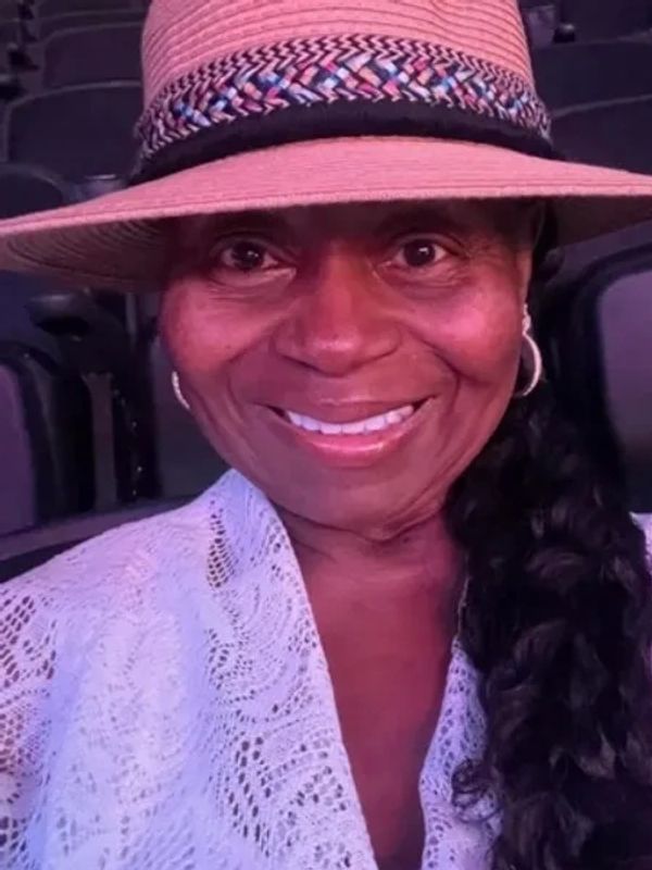 Smiling woman wearing a wide-brimmed hat and lace top.