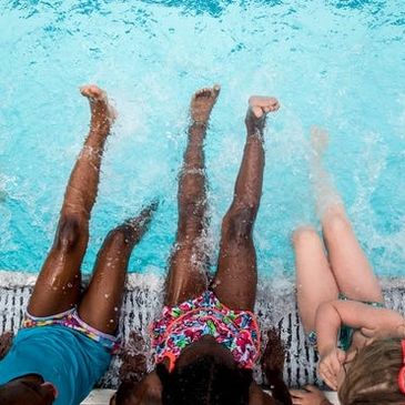 Three children splashing water with their legs at the poolside.