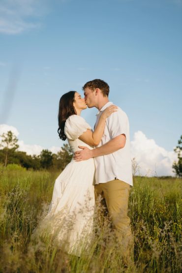 Couple kissing outdoors in a grassy field.