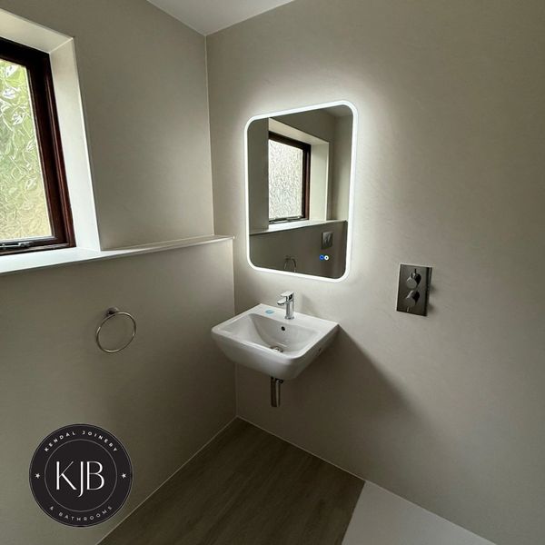 Minimalist bathroom with a modern illuminated mirror and wall-mounted sink.