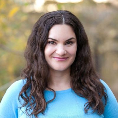 Smiling woman with long curly hair in a blue top outdoors.