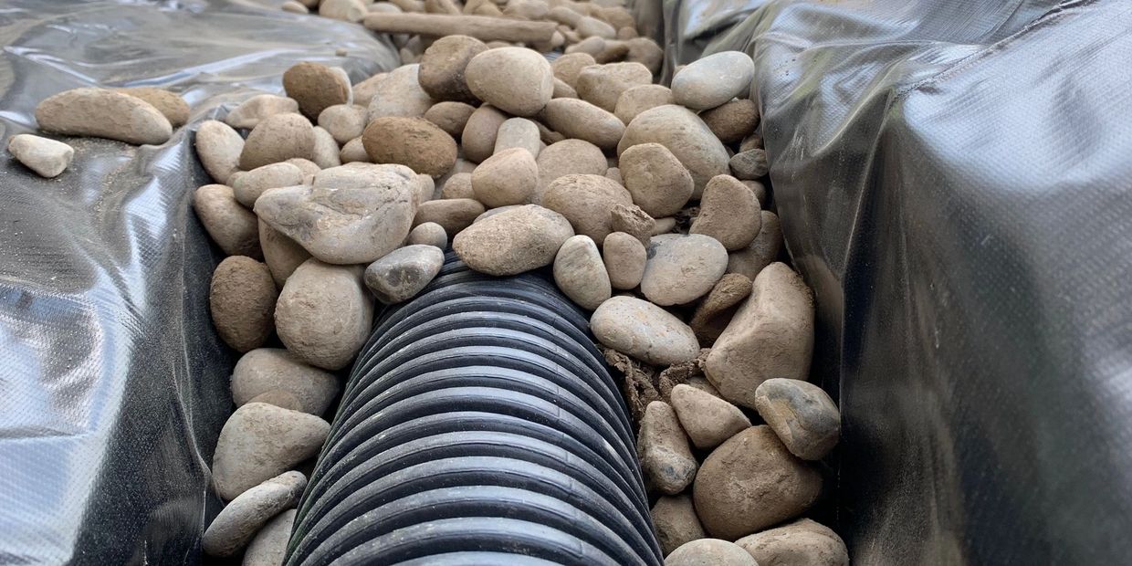 Close-up of a drainage pipe surrounded by decorative stone, designed to direct water flow and preven
