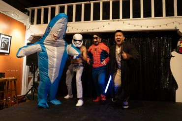Four people in costumes posing on stage, including a shark, Stormtrooper, Spider-Man, and Jedi.