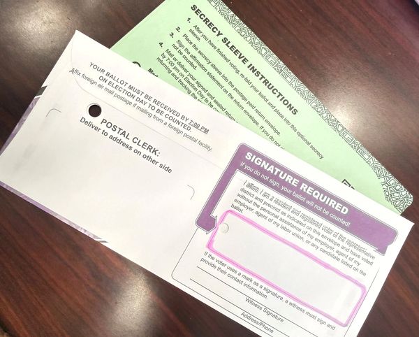 Return ballot envelope highlighting where to sign and the green secrecy sleeve that goes inside.
