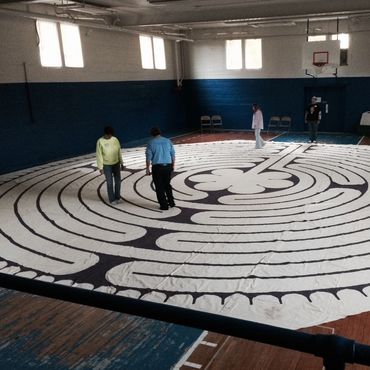 People walking on a large labyrinth pattern inside a gymnasium.