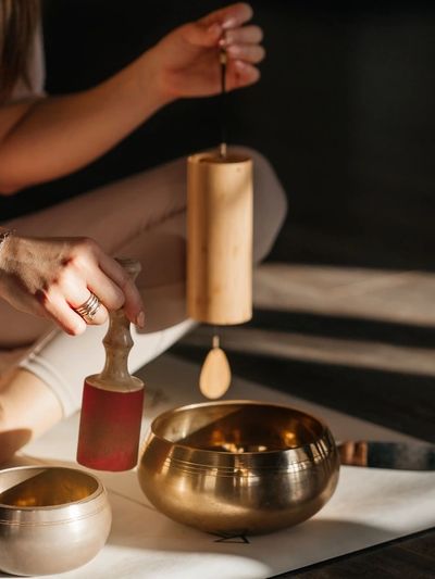 Hands playing a brass singing bowl with a wooden mallet and chime.