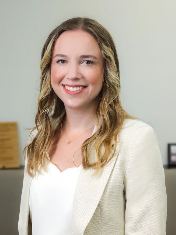 Smiling woman with wavy blonde hair in a white blazer.