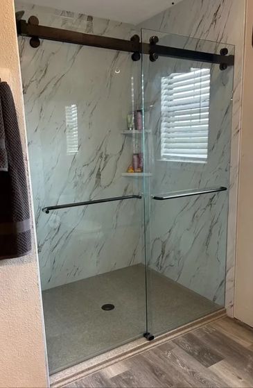 Modern glass sliding shower enclosure with marble walls and wood floor.
