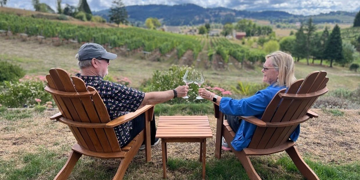 Couple enjoying wine outdoors with vineyard view.