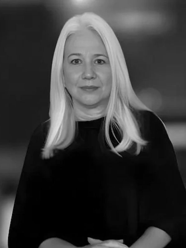 Mature woman with long white hair in black top posing indoors.