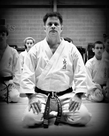 Senior martial arts instructor sitting in seiza, in black and white.