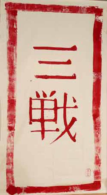 Red Japanese calligraphy on a white scroll, reading 'Sanchin' (Three Battles).