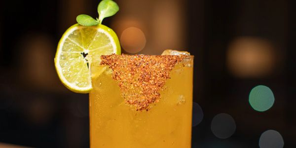 A yellow cocktail with chili salt rim and lime garnish.