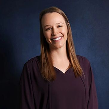 Smiling woman with long hair in a dark blouse against a blue background.