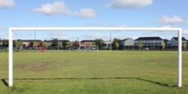 Empty soccer goalpost on a grassy field under a blue sky.