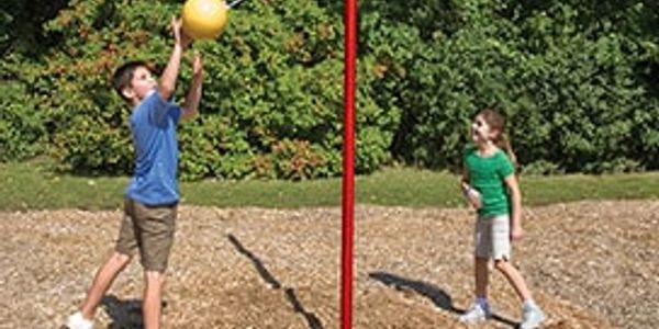 Two kids playing tetherball outdoors on a sunny day.