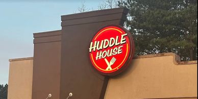 Huddle House restaurant sign illuminated against a dusk sky.