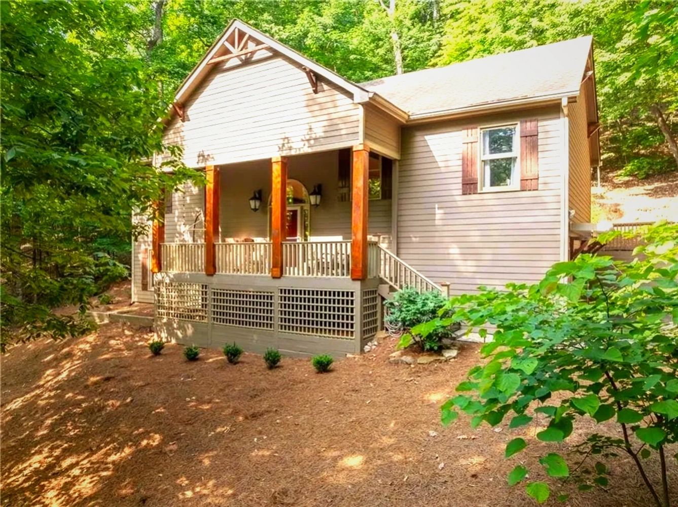 A cozy house with a porch surrounded by lush green trees.