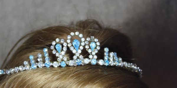 A sparkling tiara with blue and clear gemstones on blonde hair.
