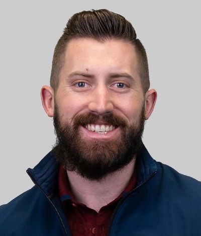 Smiling man with a beard and neatly styled hair wearing a blue jacket.