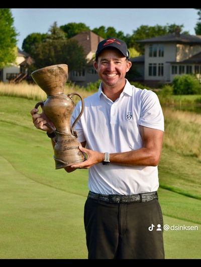 Smiling golfer holding a unique trophy on a sunny golf course.