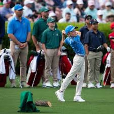 Young golfer swinging with spectators and caddies behind.
