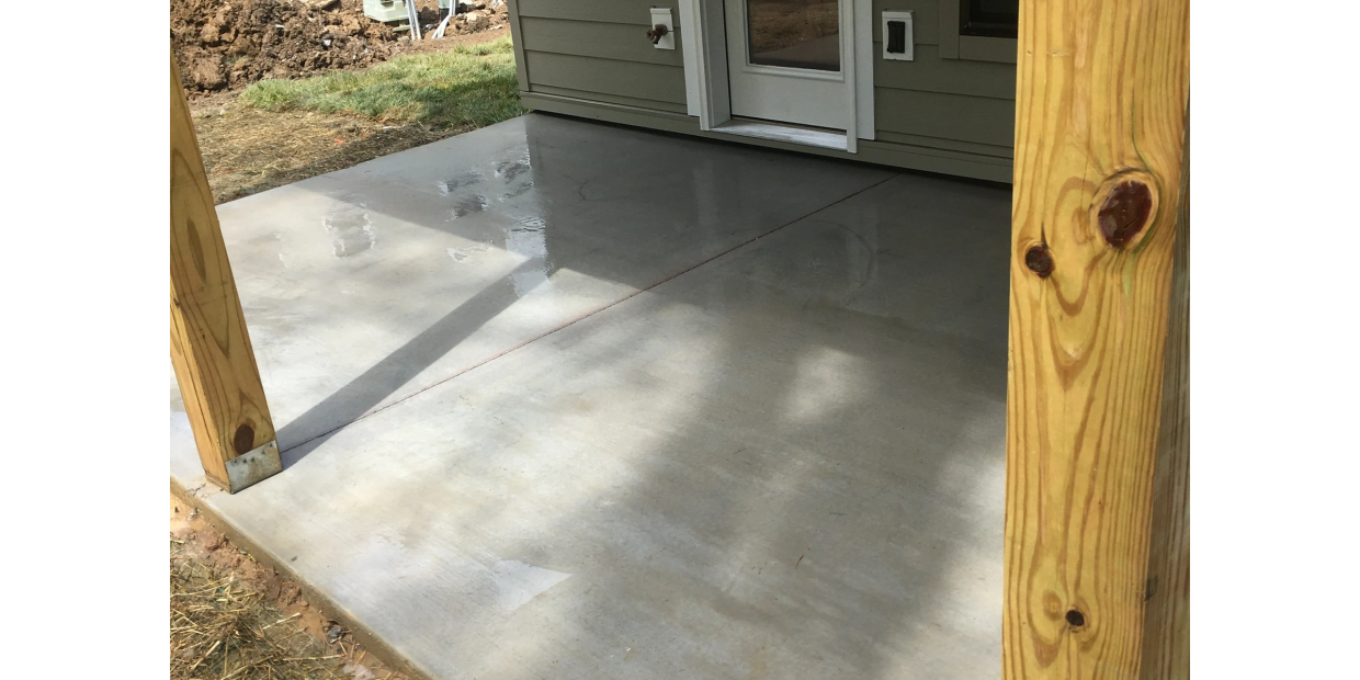 Newly poured concrete patio outside a house with wooden posts.