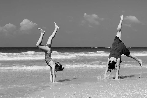 2 ladies standing on they're hands in the beach shore