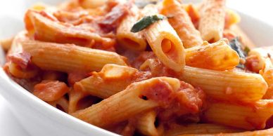 Bowl of penne pasta with tomato sauce and herbs.