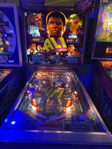 Illuminated Ali-themed pinball machine with vibrant artwork and lights.