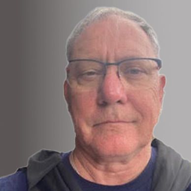 Portrait of an older man with glasses against a gray gradient background.