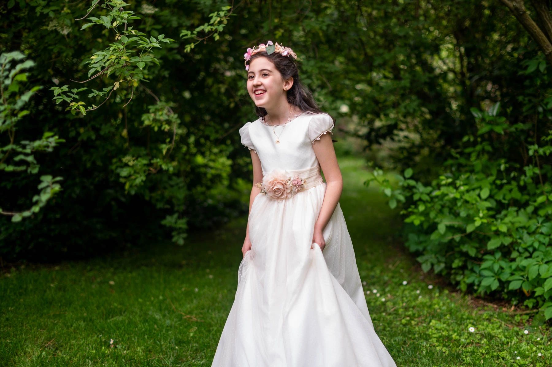 A joyful girl in a white dress with floral accents in a lush garden.