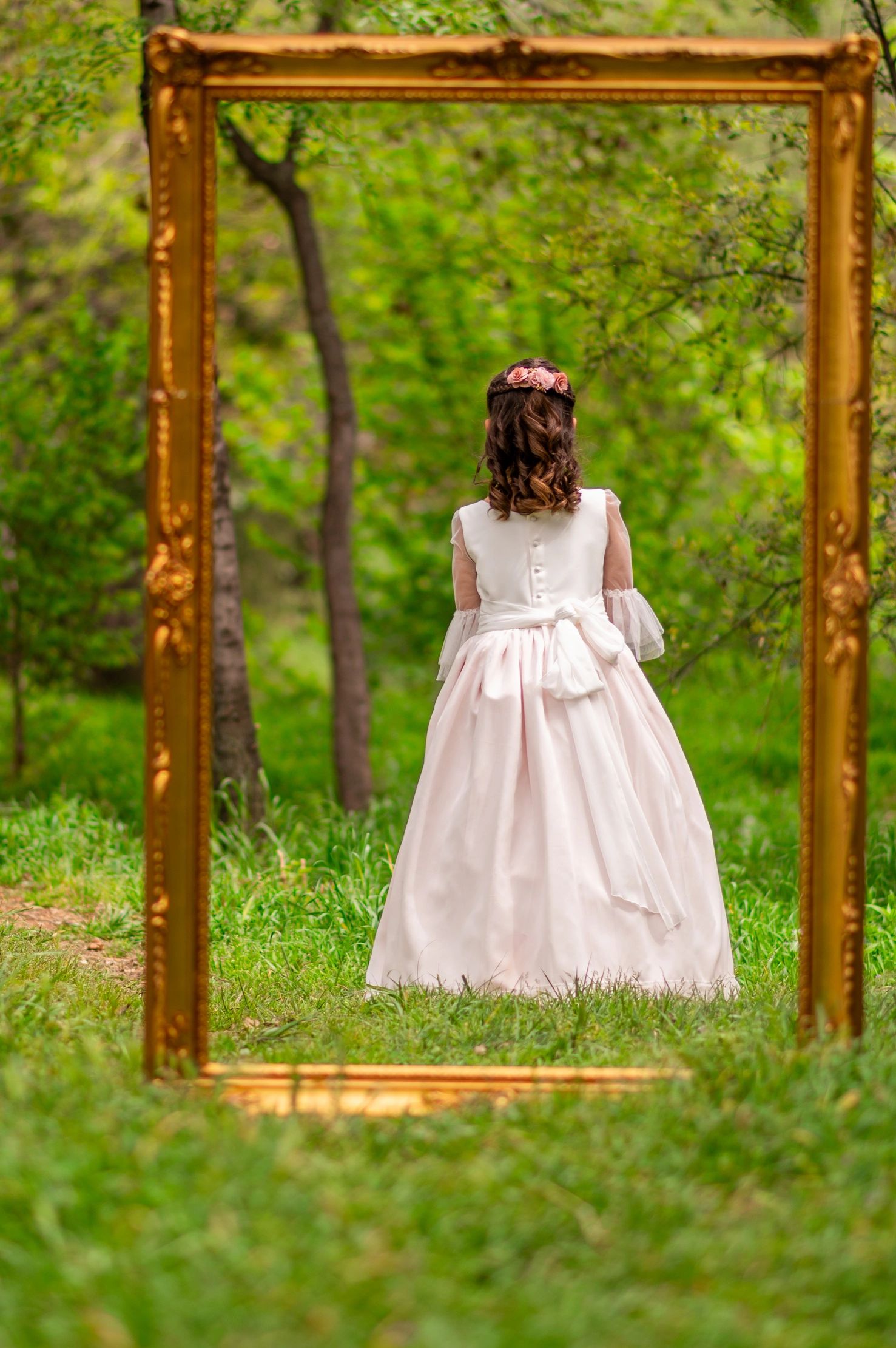 Niña de espaldas vista a través de un marco dorado en un bosque.