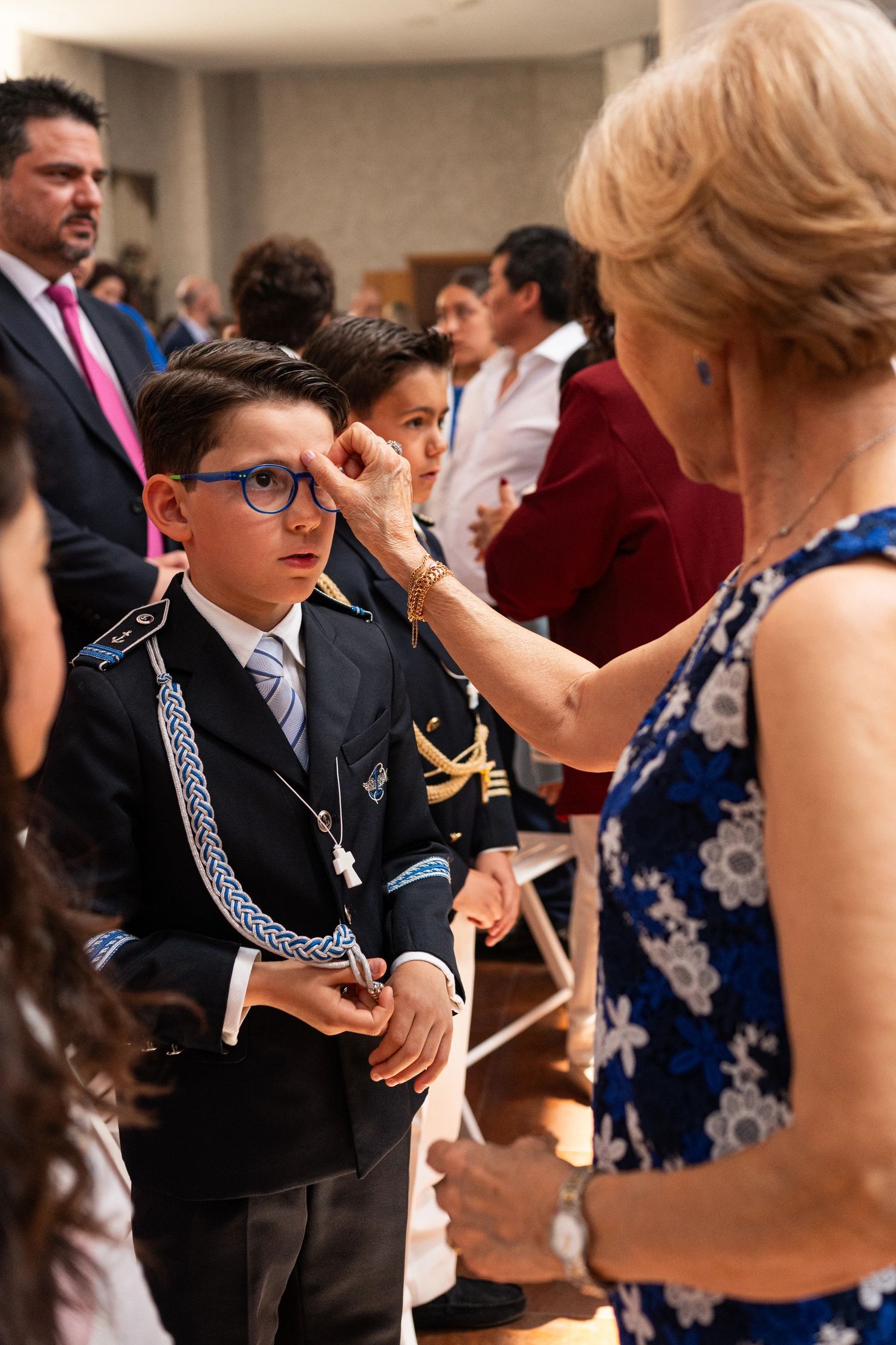 Boy in formal attire receiving a blessing from an older woman during a ceremony.